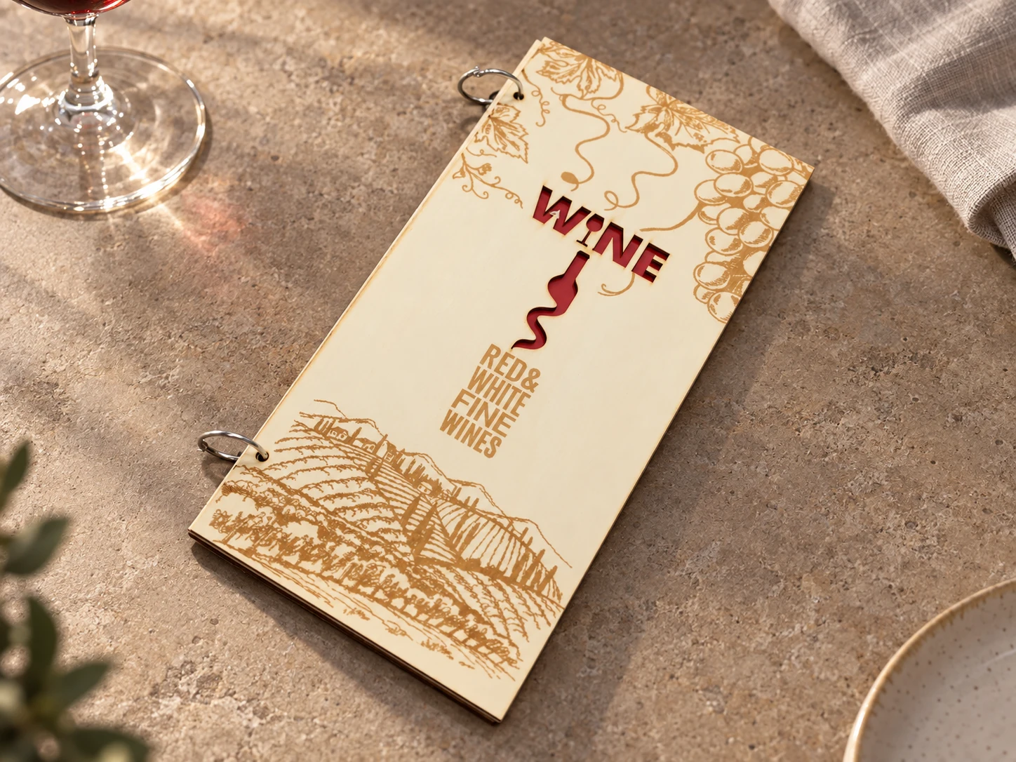 Copertina in legno della carta vini con anelli, incisione di vigneti e scritta WINE traforata · mockup ambientato
