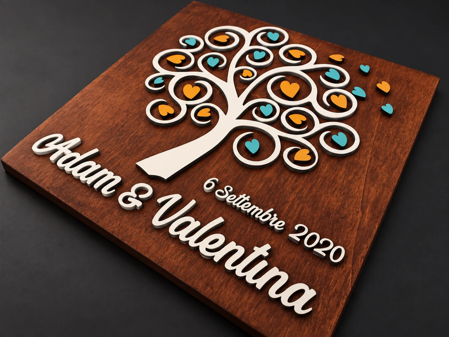 Pannello in legno scuro con albero chiaro, cuori colorati e nomi Adam e Valentina